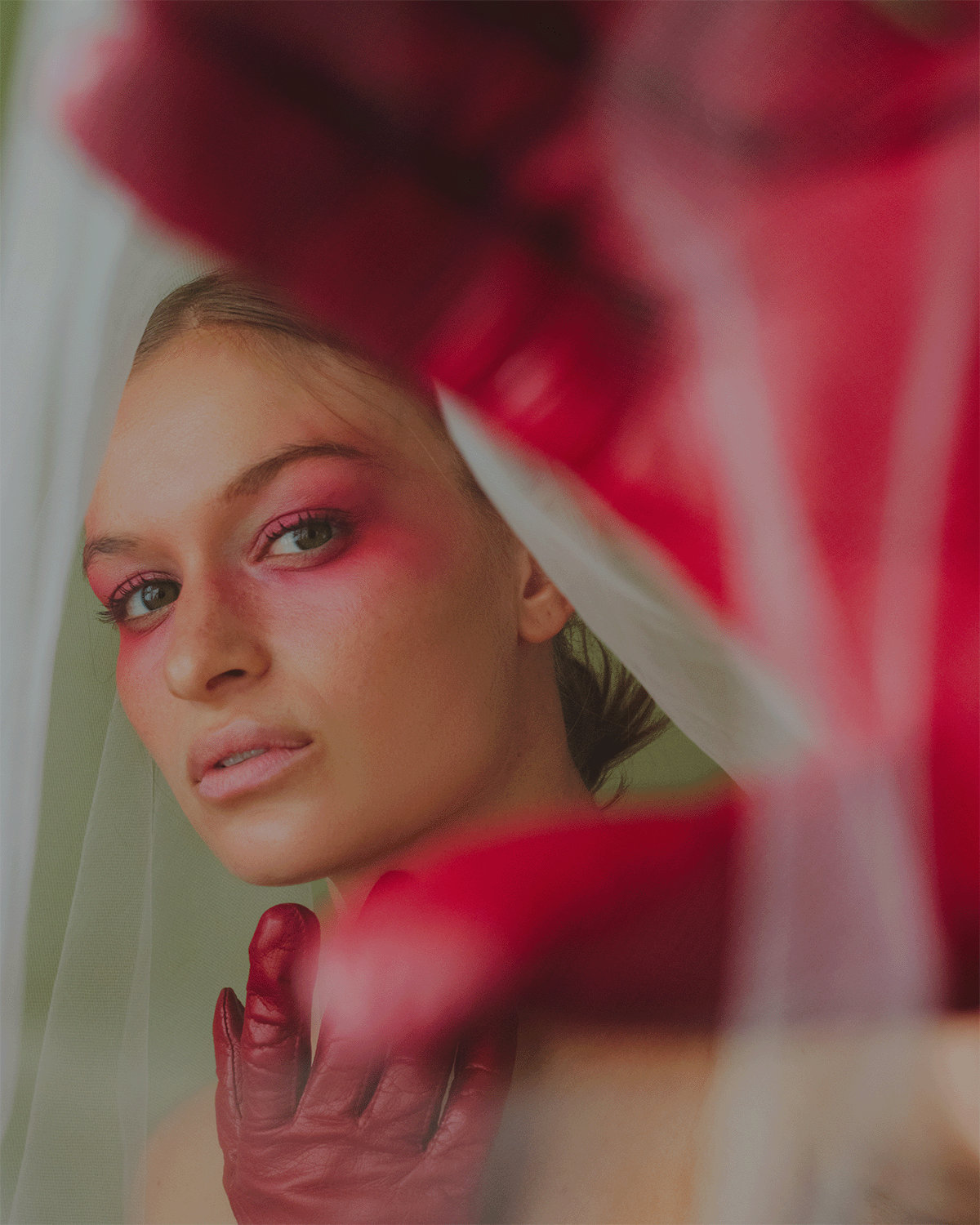 Kayse posing with red gloves framing her face towards the edge of the camera with her red faded makeup starting at her eyes and reaching towards the edges of her face.