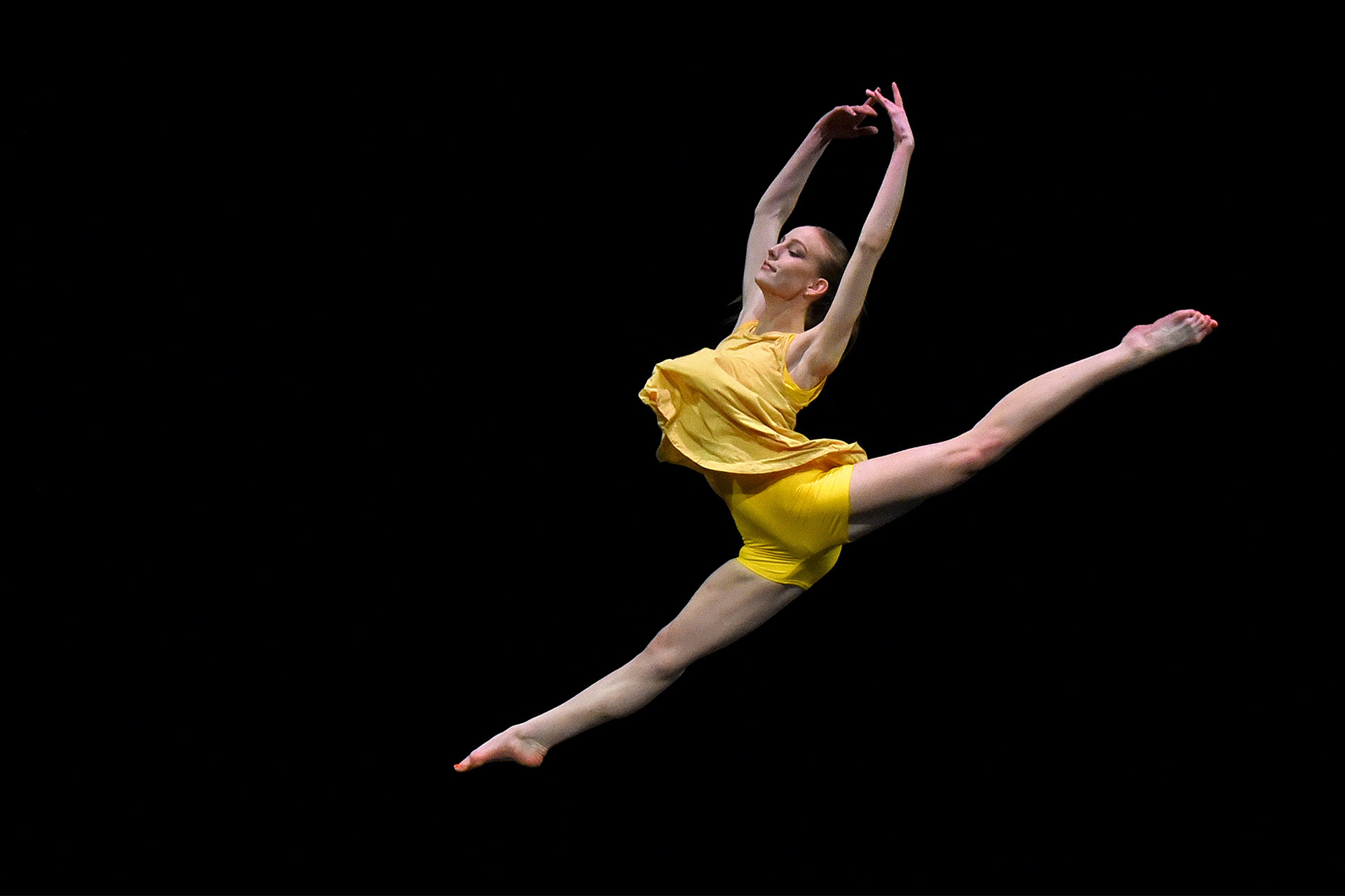 A dancer in a yellow stage costume leaping