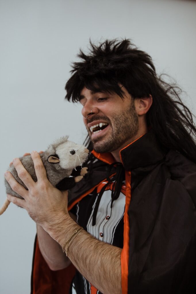Justin Darnell posing with a stuffed possum while wearing a black wig and vampire cape by Justin Murphy Justin Darnell posing with a stuffed possum while wearing a black wig and vampire cape