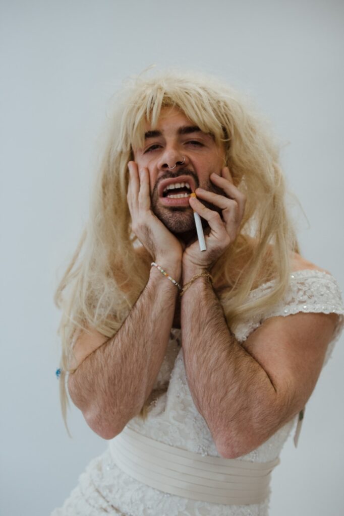 Justin Darnell posing with a blonde wig and cigarette while wearing a white dress by Justin Murphy Justin Darnell posing with a blonde wig and cigarette while wearing a white dress